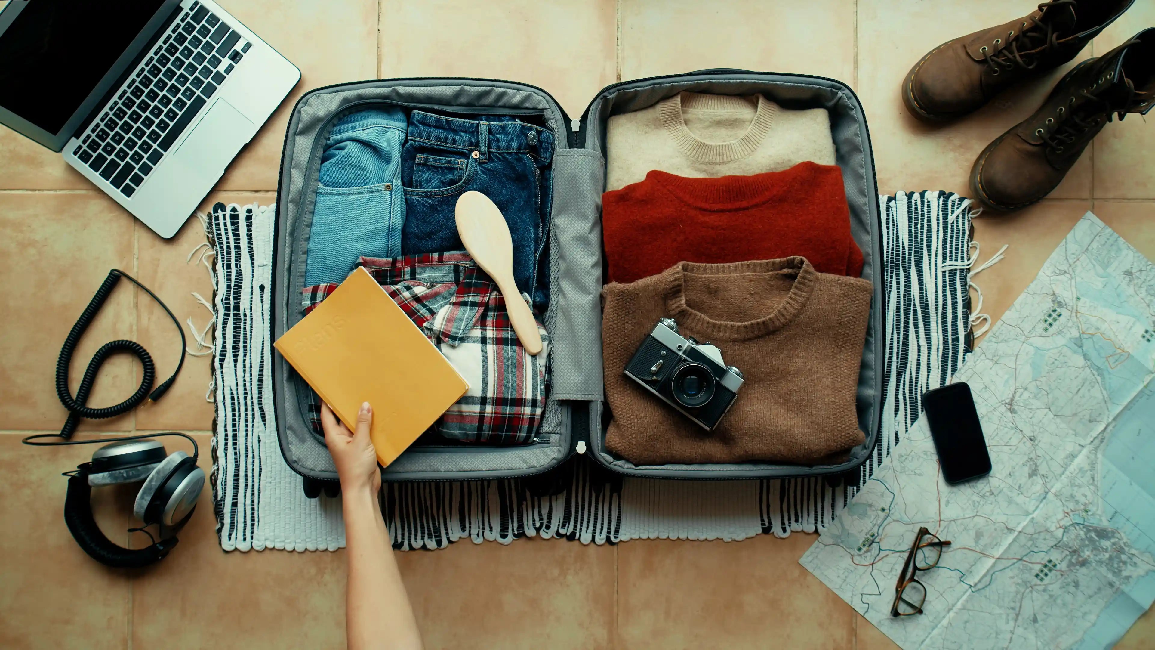 En åpen koffert med klær, kart, mobiltelefon, kamera, laptop og hodetelefoner.
