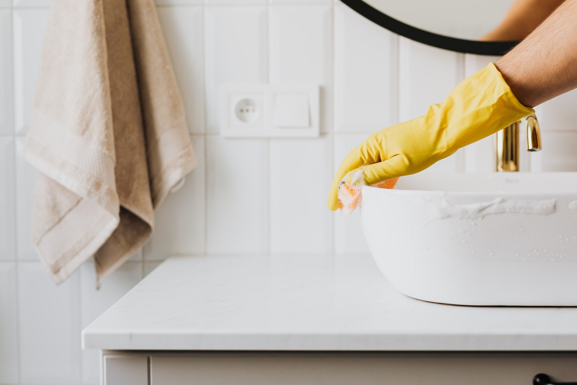 En person som vasker vasken på et bad med såpe, svamp og gule hansker på.