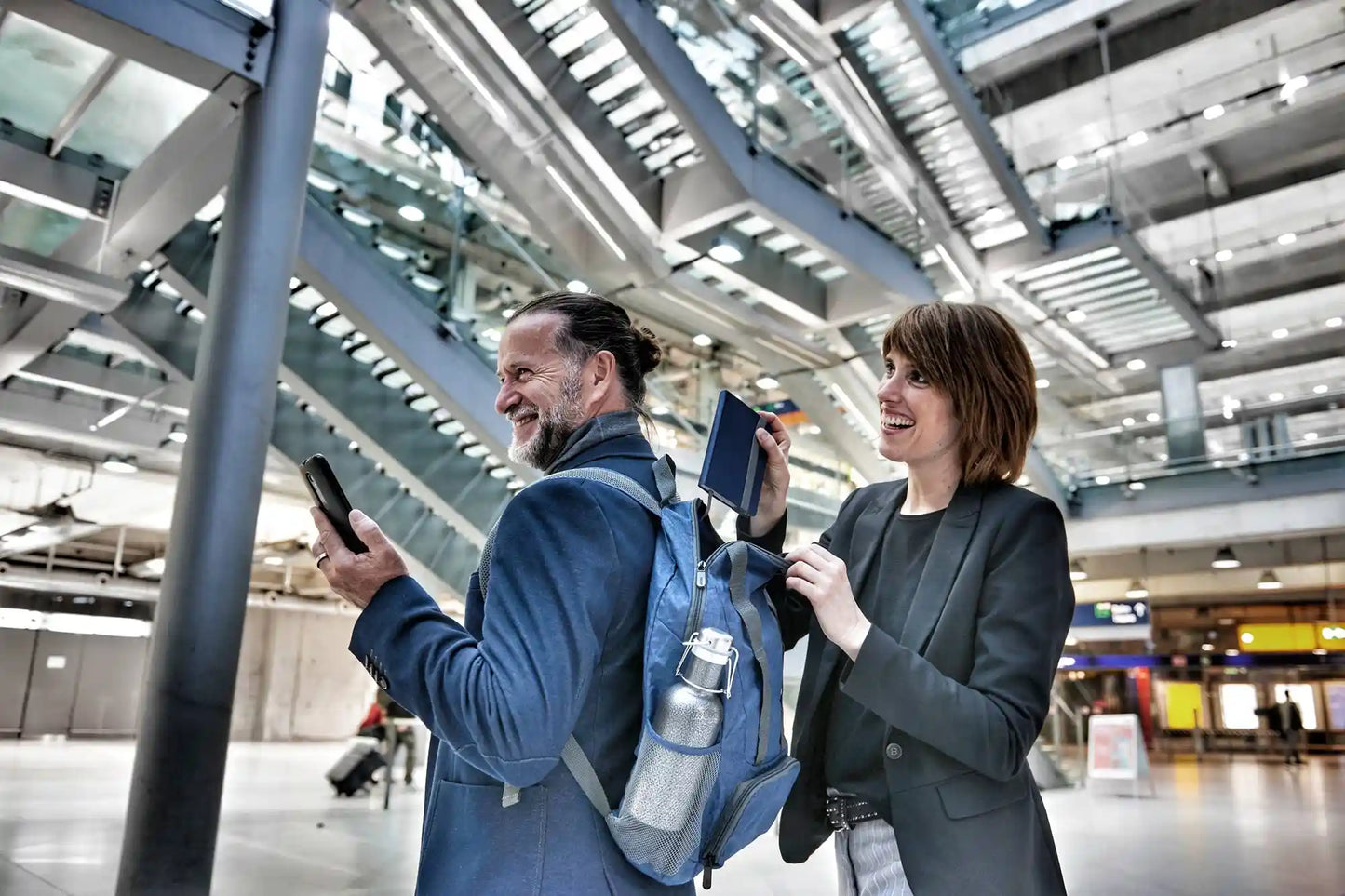 En mann og en dame på flyplassen der mannen har på seg en blå sammenleggbar ryggsekk